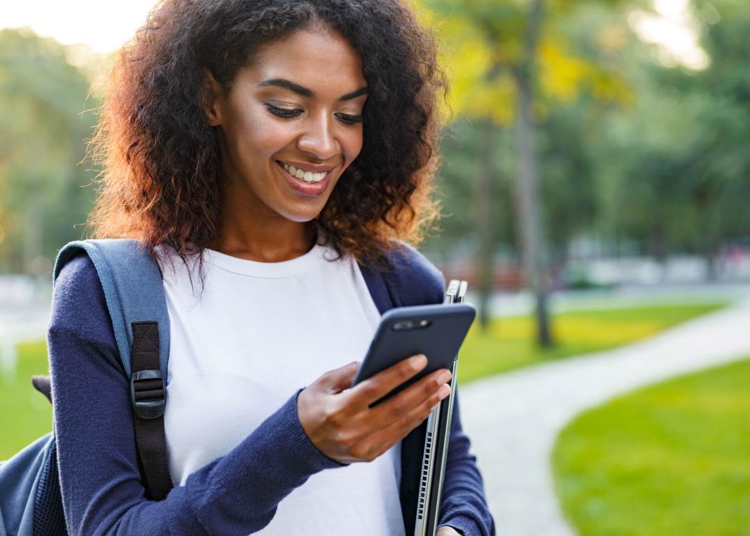 fille dans un parc qui regarde son téléphone avec un ordinateur dans l'autre